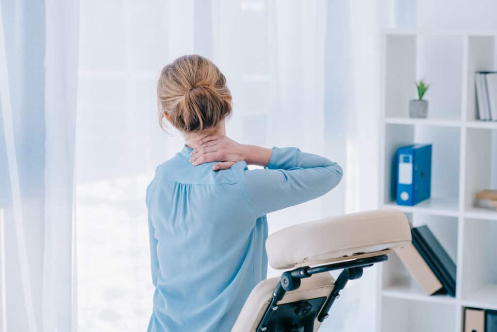neck pain in woman with blonde hair next to chiropractic chair