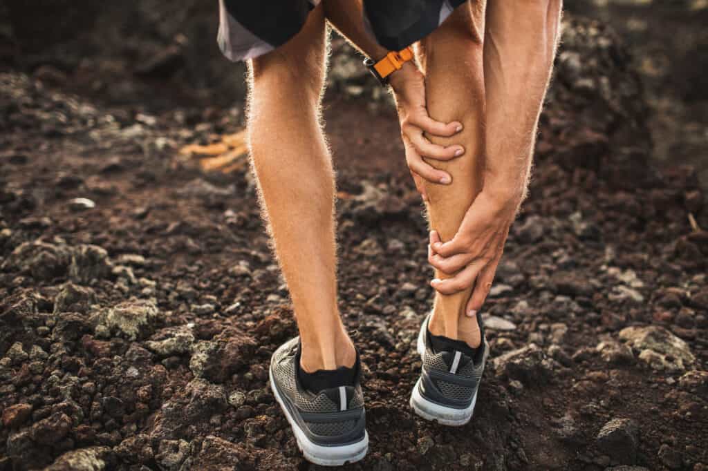 Male runner holding injured calf muscle and suffering with achilles tendon pain. Sprain ligament while running outdoors. View from the back close-up.
