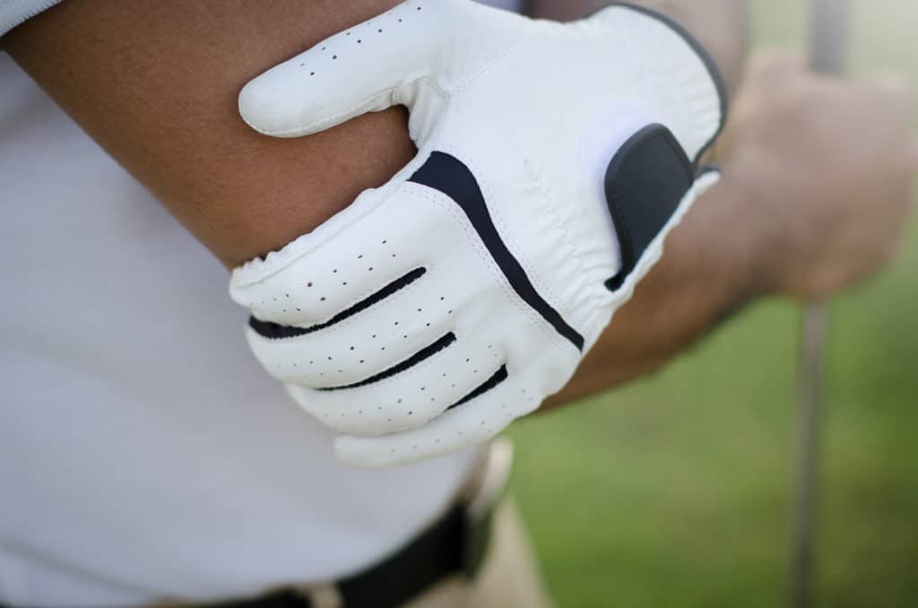 Golfer holding his elbow in pain due to golfer's elbow 