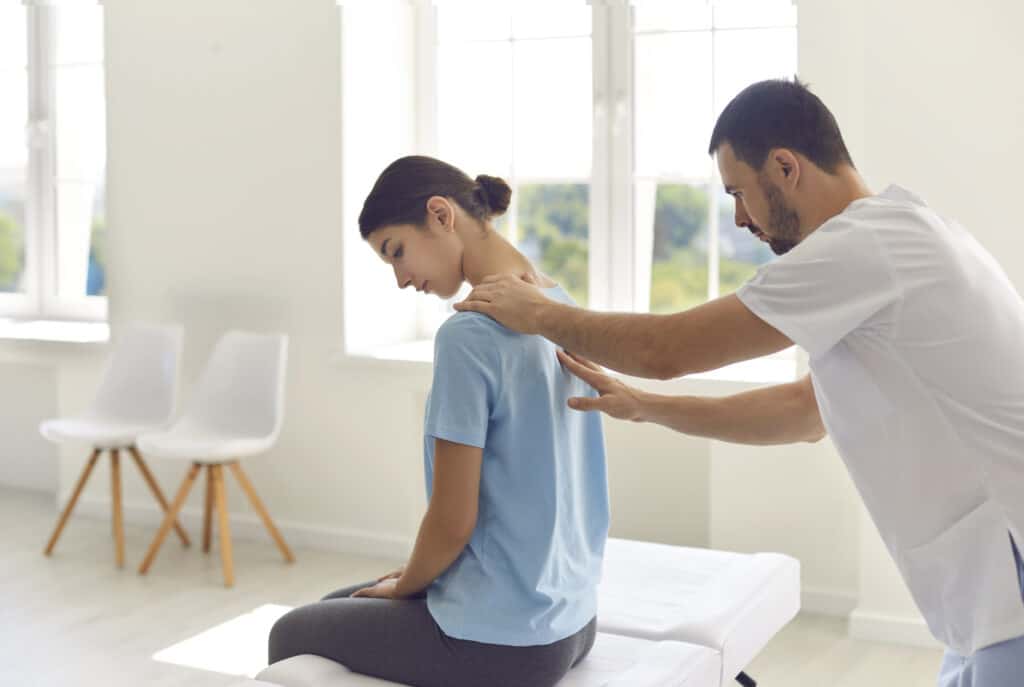 Male chiropractor curing client's backache in new chiropractic clinic or health center. Licensed physician, doctor of osteopathic medicine, helping young woman with scoliosis by making early diagnosis