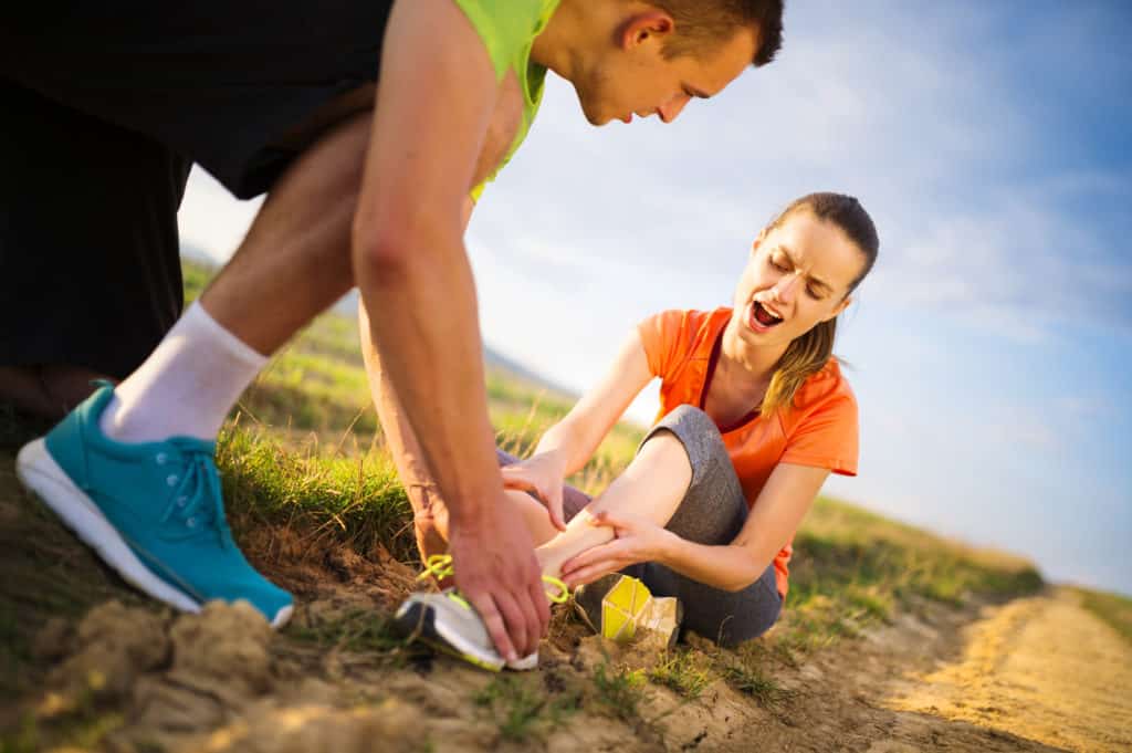 Woman suffering from sports injury caused by running being helped by sports man