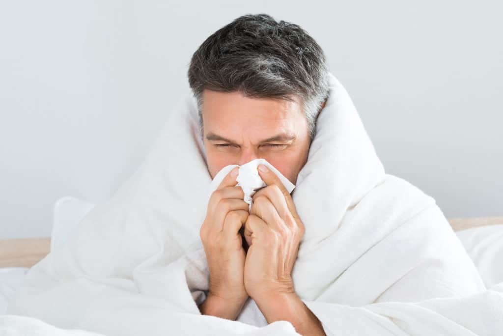 Man sitting on bed blowing his nose due to the flu he has 