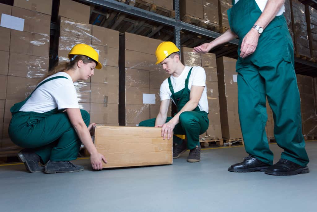 Two young workers lifting heavy box in warehouse