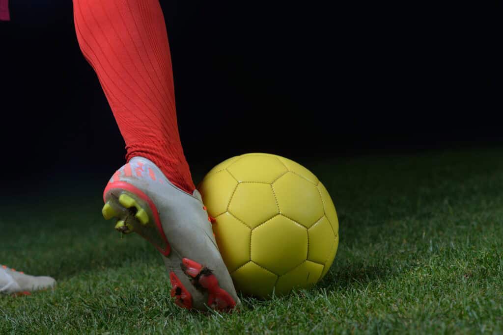 soccer player kicking yellow ball
